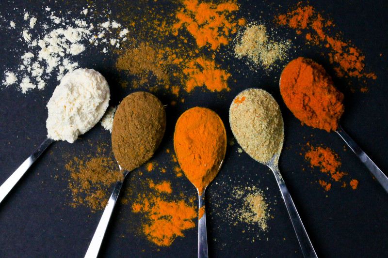 Spoons of ground spices fanned out on a dark navy surface.